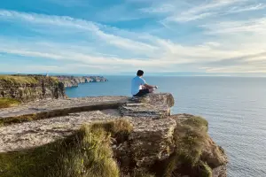 Turista aproveitando dia de sol nos Cliffs of Moher durante verão irlandês.