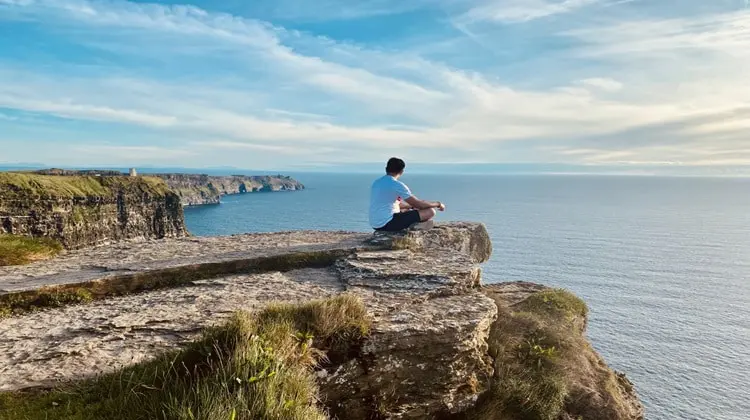 Turista aproveitando dia de sol nos Cliffs of Moher durante verão irlandês.