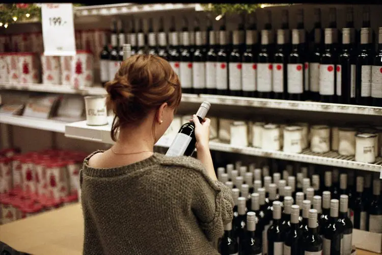 Mulher no supermercado lendo o rótulo de um vinho