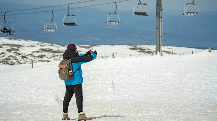 Homem de casaco azul tira foto na neve na Serra da Estrela