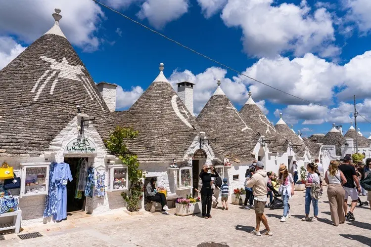 Turistas passeando pela região do centro turístico de Alberobello em dia de céu azul na Itália.