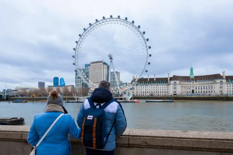 Visitar o London Eye Dois turistas admirando o London Eye de longe.