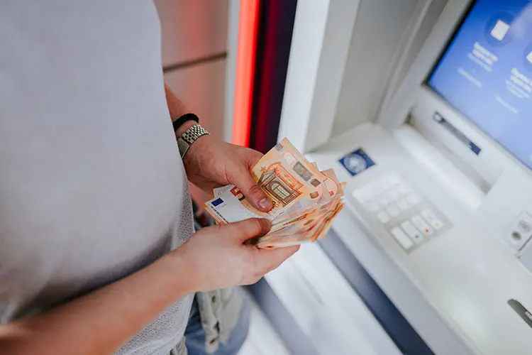 Pessoa retirando notas de euro em caixa eletrônico no exterior.