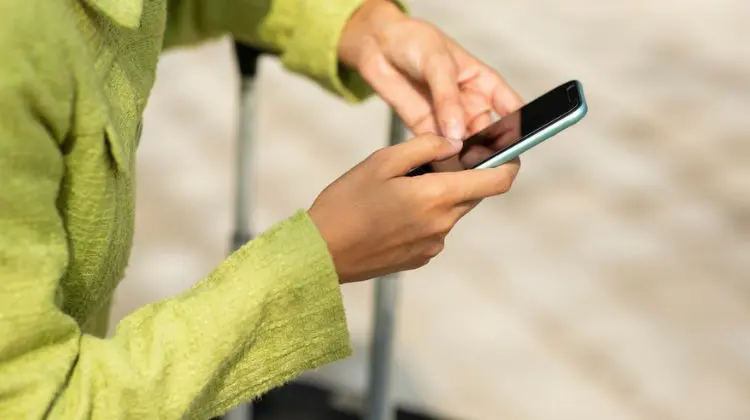 Pessoa usando celular com conexão da A Casa do Chip ao lado de uma mala de viagem