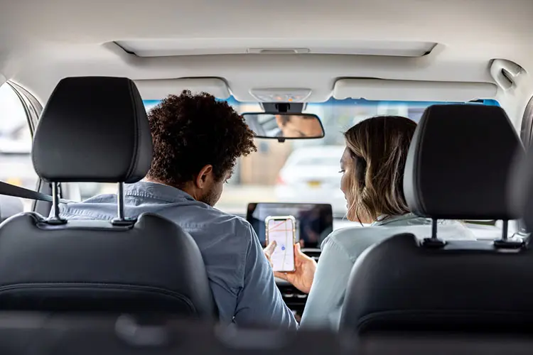 Momondo é confiável para alugar carro, com casal utilizando celular no interior de um carro.