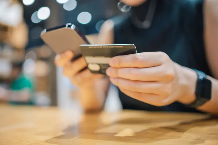 Mulher segurando cartão e celular para comprar euro