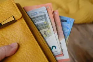 Mão segura carteira amarela com cédulas de euro à mostra