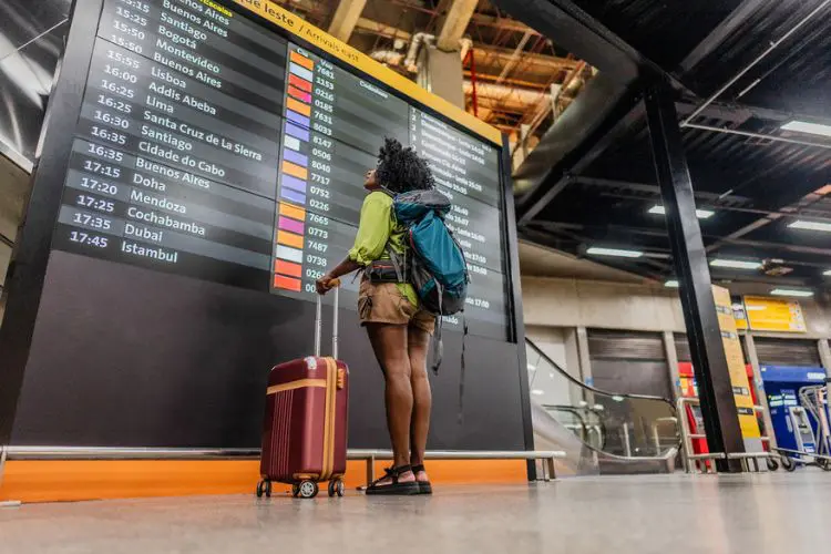 Mulher com mochila observando painel de voos em aeroporto.