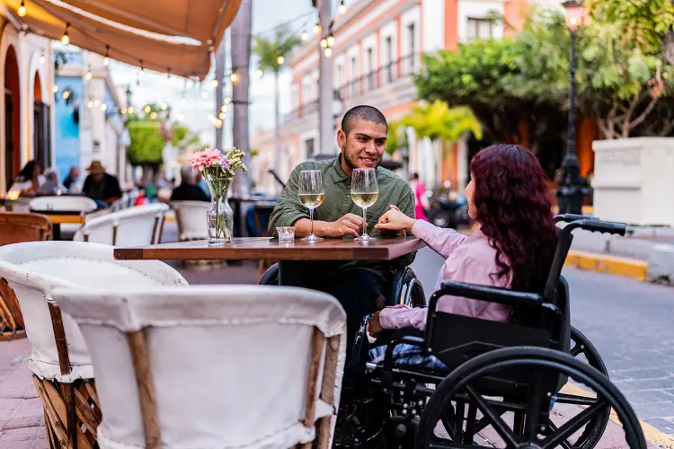 Casal portando cadeira de rodas em mesa de restaurante ao ar livre