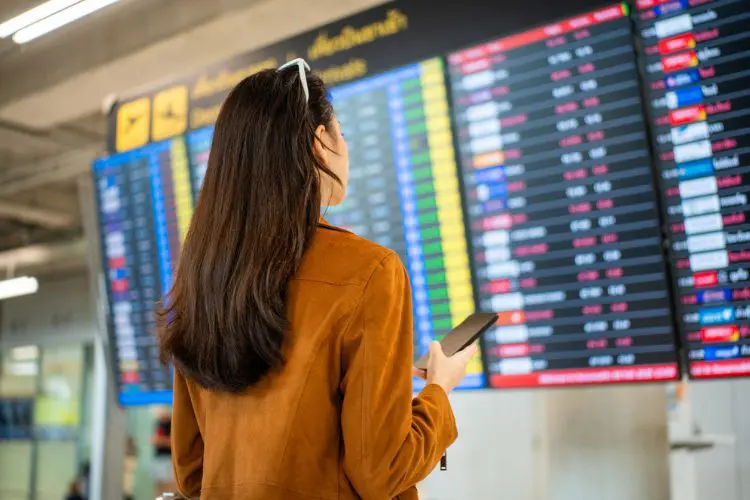 Mulher observa painel de voos em aeroporto antes de embarcar.
