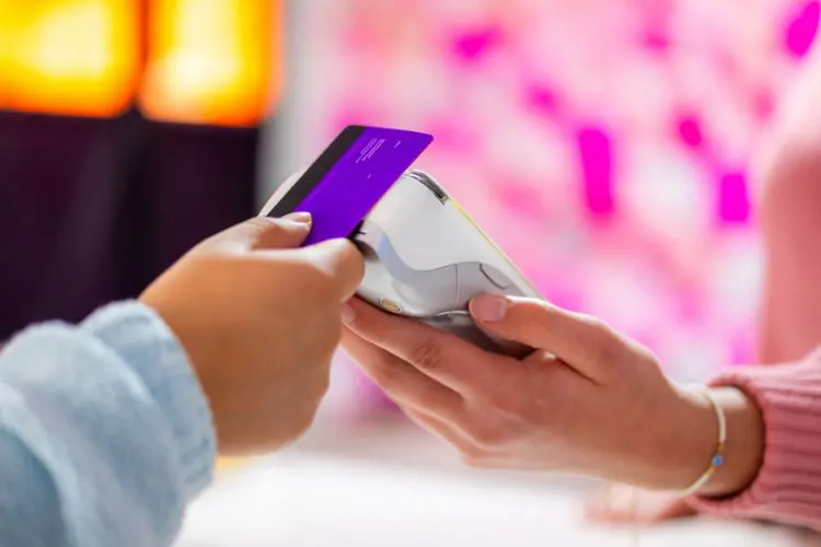 Pessoa realizando pagamento por aproximação com um cartão Nubank Ultravioleta Conta Global em uma maquininha de cartão