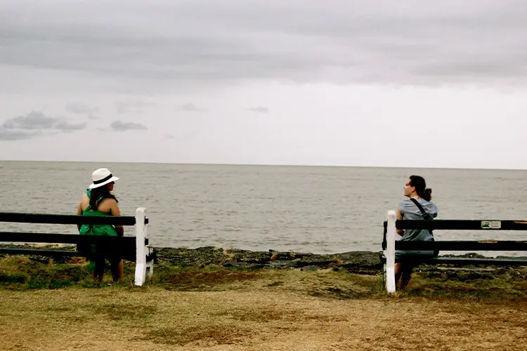 Duas mulheres sentadas, cada uma em um banco, contemplando o mar