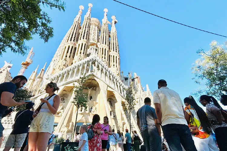Turistas em frente a Sagrada Família em dia de muito sol em Barcelona.