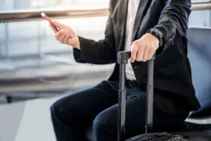 Homem com mala em aeroporto usando celular com Claro Passaporte