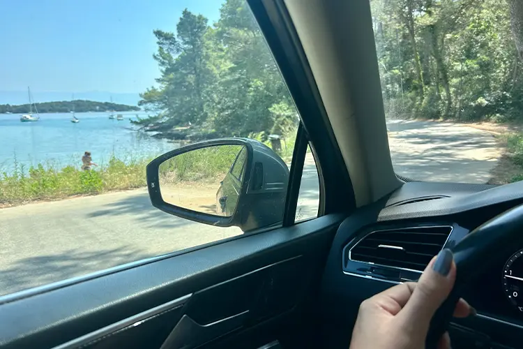 mão de mulher no volante de carro com mar ao fundo