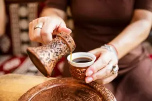 Mulher servindo café em itens típicos da Bósnia feitos de cobre