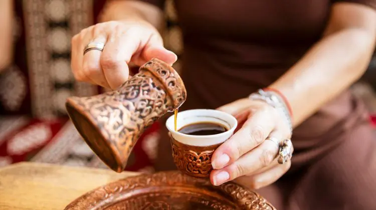 Mulher servindo café em itens típicos da Bósnia feitos de cobre