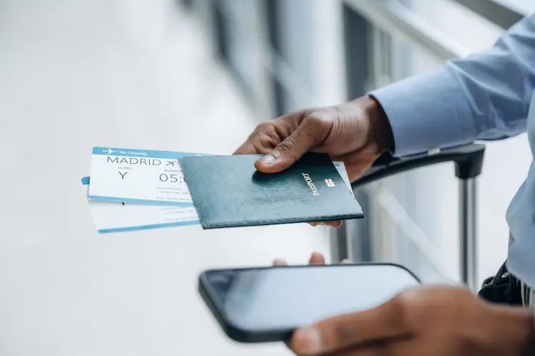Pessoa segura passaporte com cartão de embarque para Madrid, ao lado de um celular.