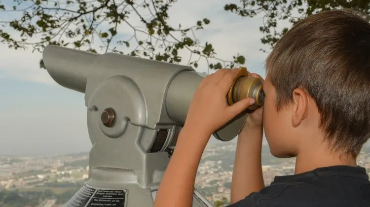 criança observando cidade a partir de telescópio