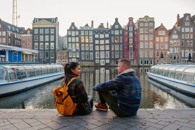 Casal admira barcos de passeio no canal de Amsterdam.
