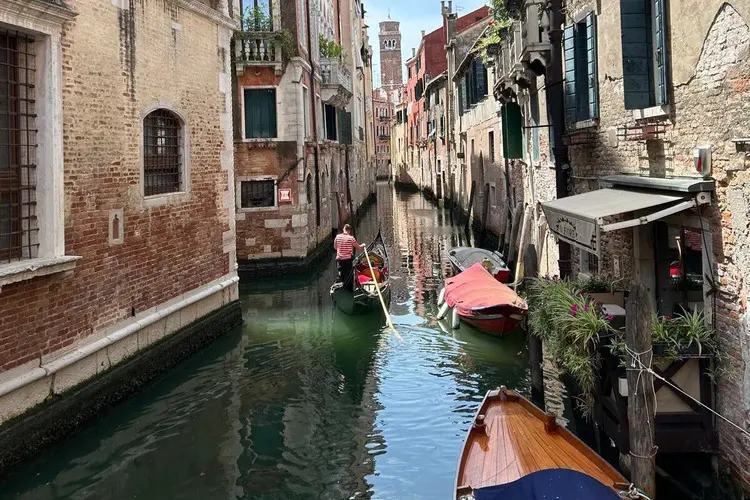 Canal estreito em Veneza com gôndolas estacionadas e em movimento.
