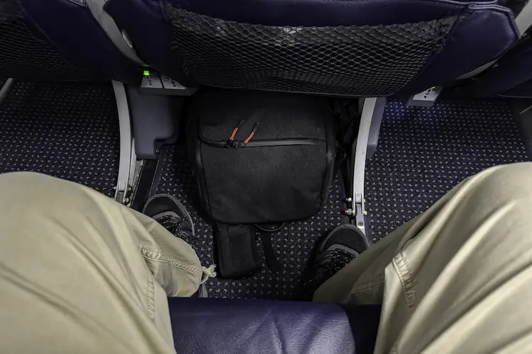 Mochila preta acomodada embaixo do assento de avião.