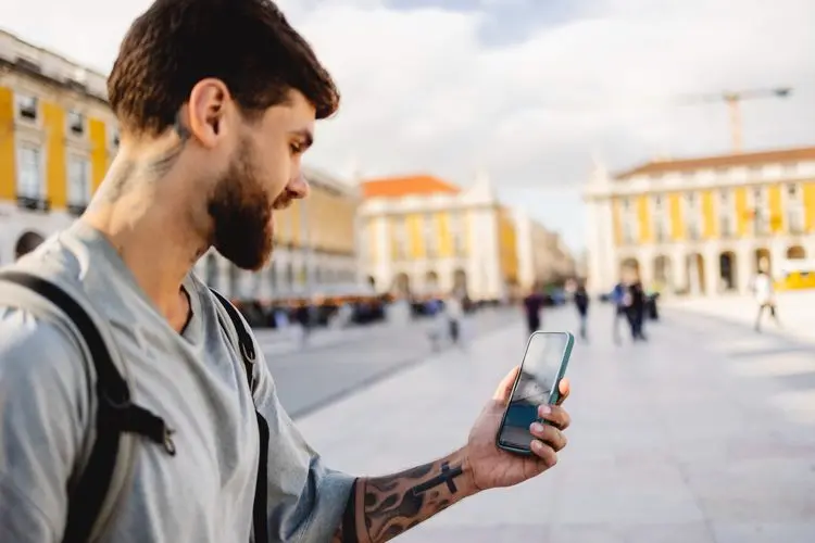 Homem segurando o celular em ponto turístico de Portugal, em dia nublado.