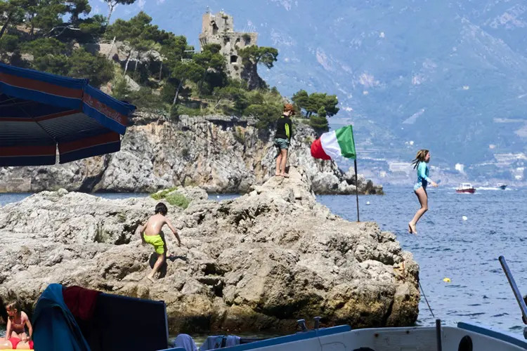 Crianças pulando no mar em praia italiana.