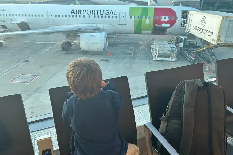 Uma criança de costas, observa um avião na pista do aeroporto de Lisboa simbolizando a jornada de uma mãe ao voar sozinha com crianças pequenas