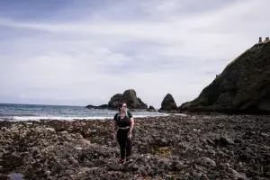 Mulher com mochila em frente a rochas e mar da Escócia.