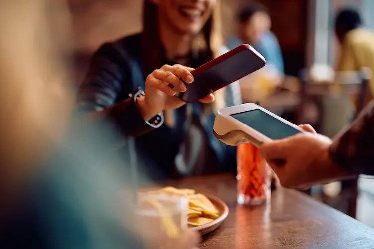 Pessoa realizando um pagamento por aproximação usando o celular em um restaurante.