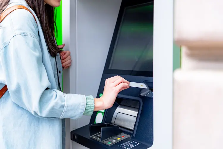 Pessoa sacando dinheiro em um caixa eletrônico usando um cartão físico da Revolut para viagem.