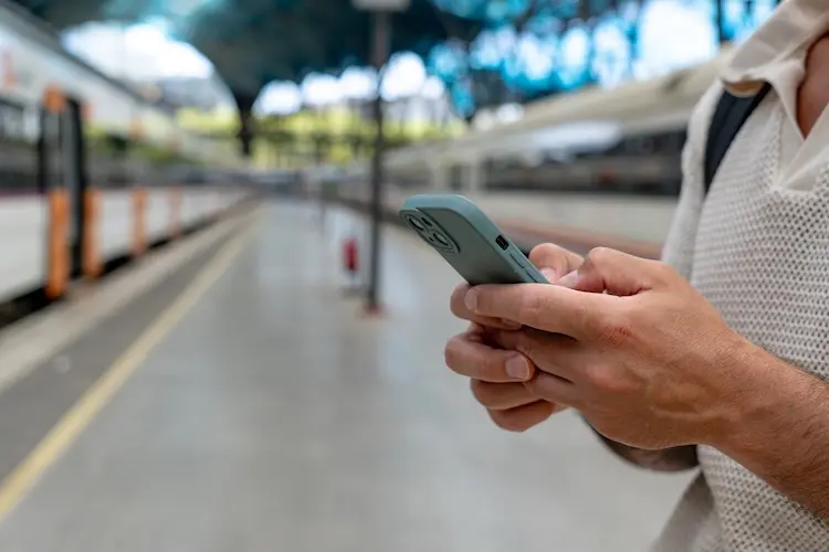 Pessoa segura um celular enquanto espera o trem em uma estação coberta.