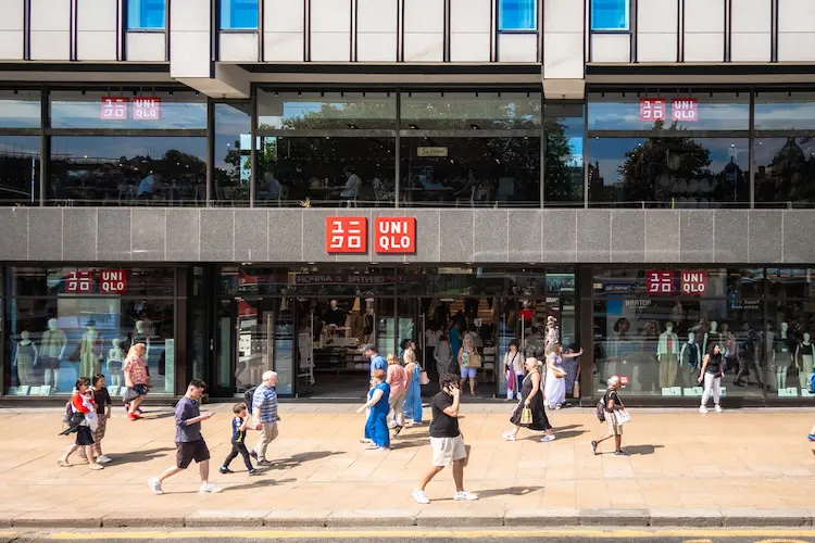 Fachada de loja de roupas Uniqlo na Europa, com pedestres caminhando pela calçada em frente ao estabelecimento.