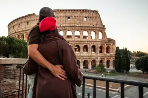 Casal de turistas apreciando a vista do Coliseu de Roma em dia nublado.