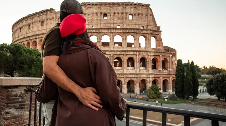 Casal de turistas apreciando a vista do Coliseu de Roma em dia nublado.