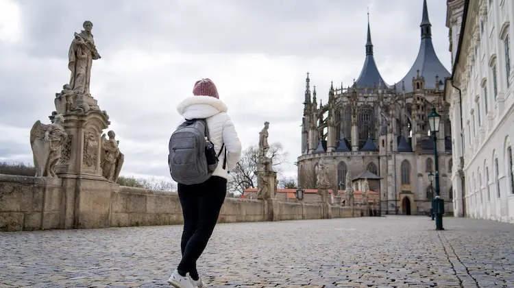 Turista de costas caminhando em rua histórica em direção à Catedral de Santa Bárbara, na República Tcheca.