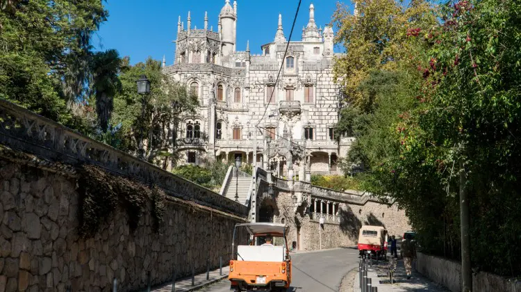 Rua em Sintra com castelo ao fundo e carros passando em um bate e volta de Lisboa.