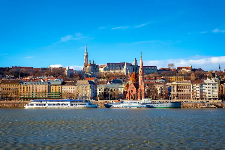 Vista panorâmica das margens do rio Danúbio com edifícios históricos e barcos em Budapeste.